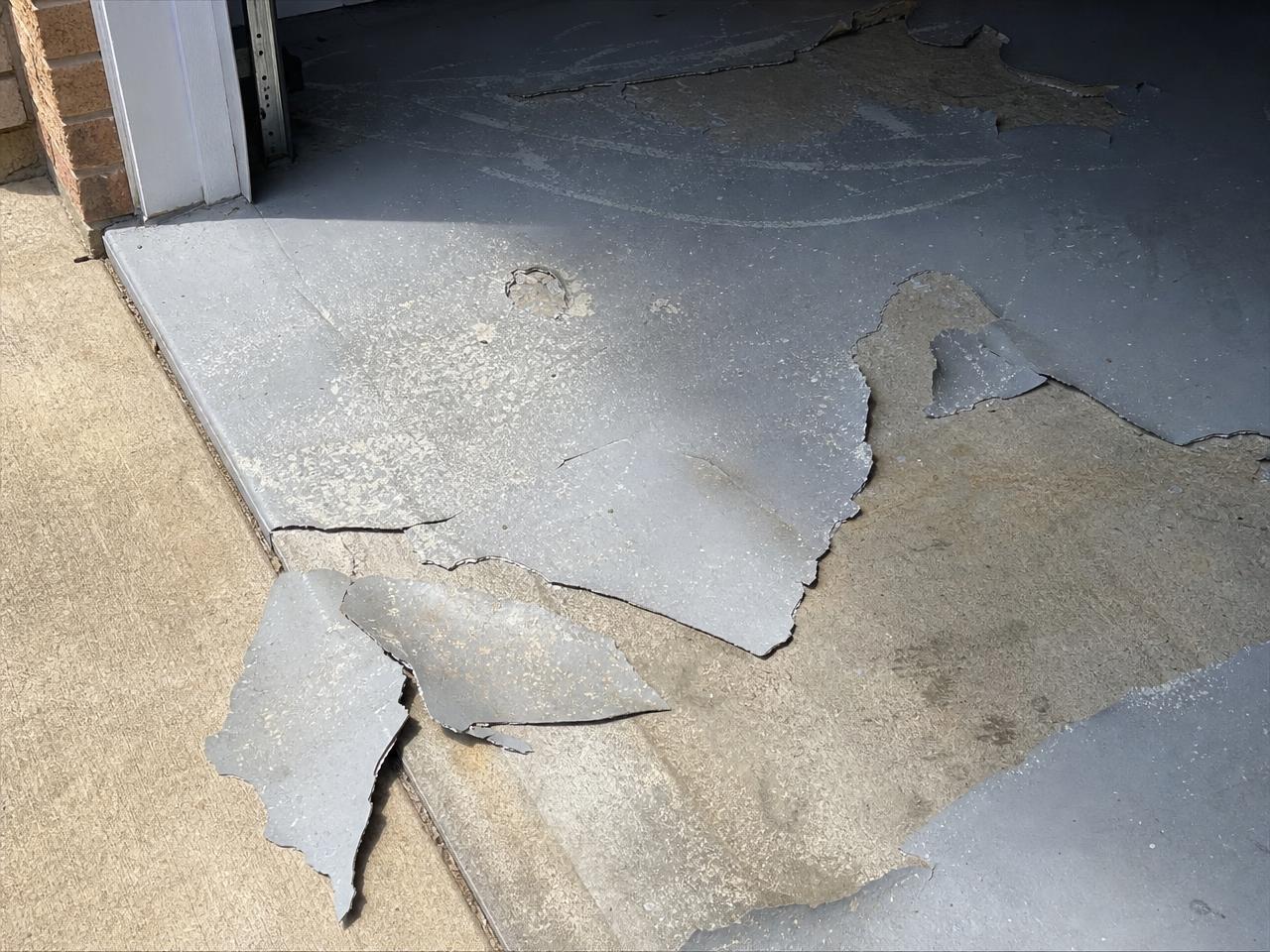 Peeling epoxy coating lifting away from a concrete garage slab