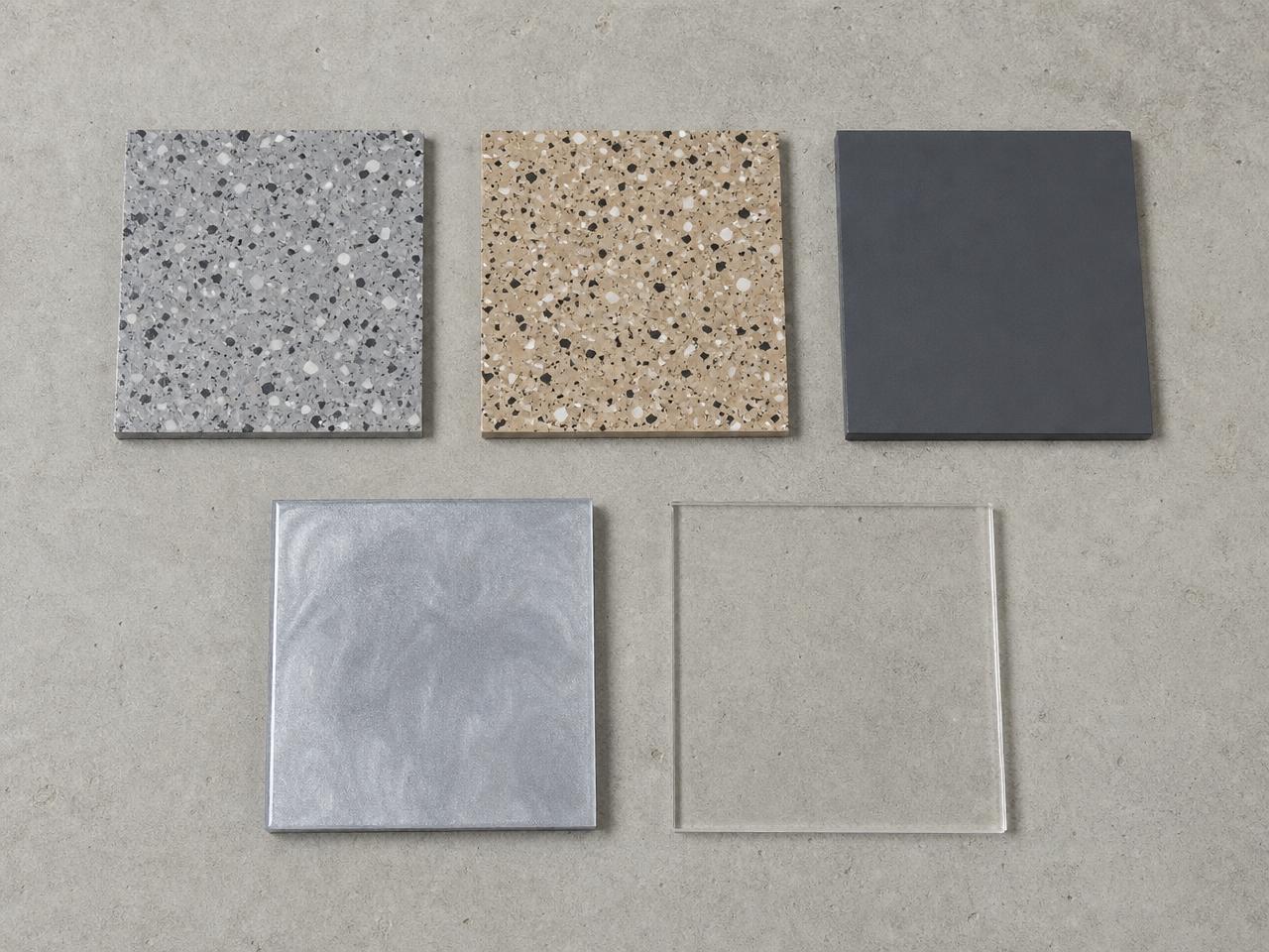 Coating sample chips in gray flake, tan flake, solid charcoal, metallic, and clear sealer finishes laid on a concrete slab