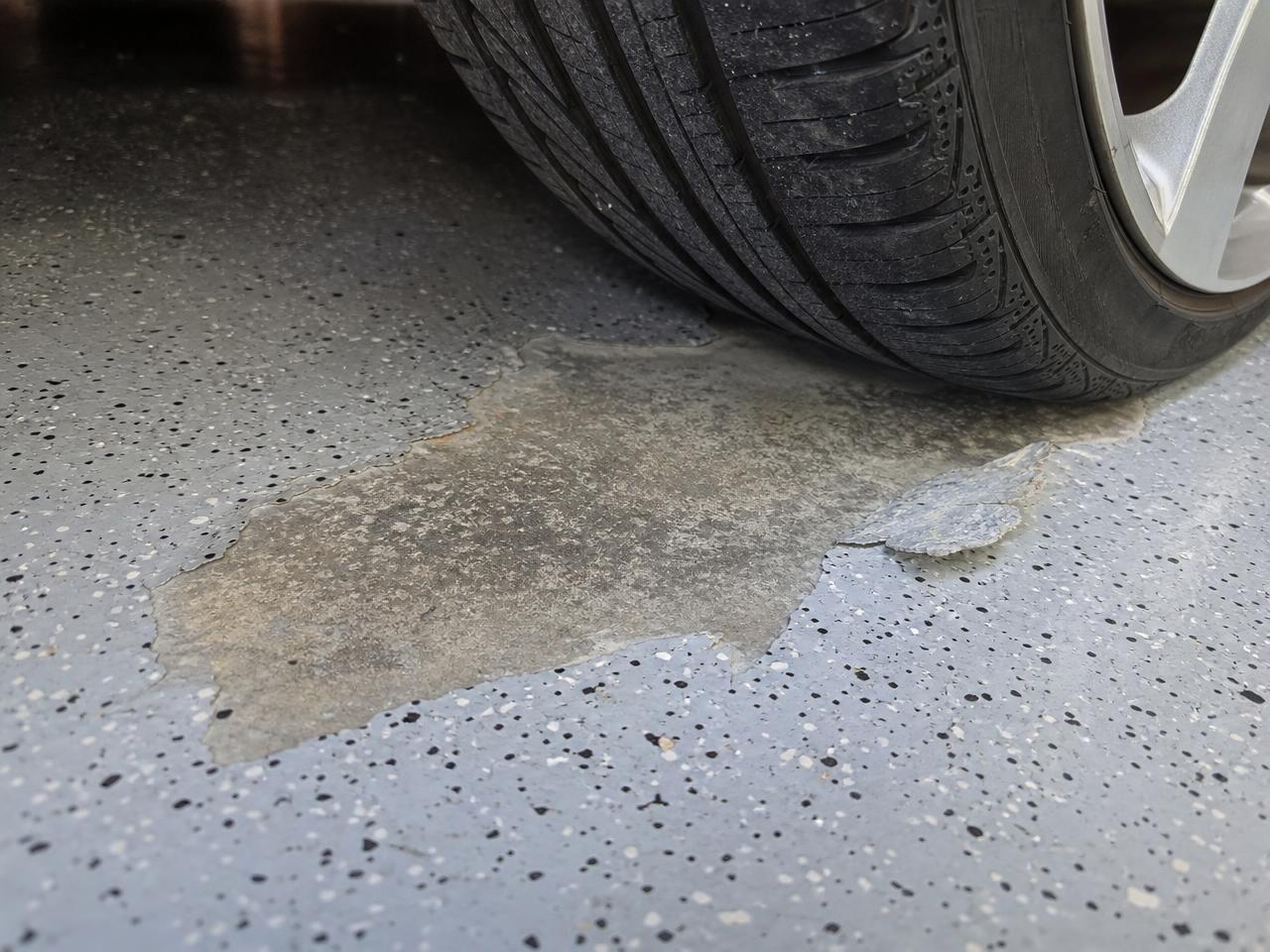 Car tire on a coated garage floor beside a patch of coating lifted by hot tire pickup