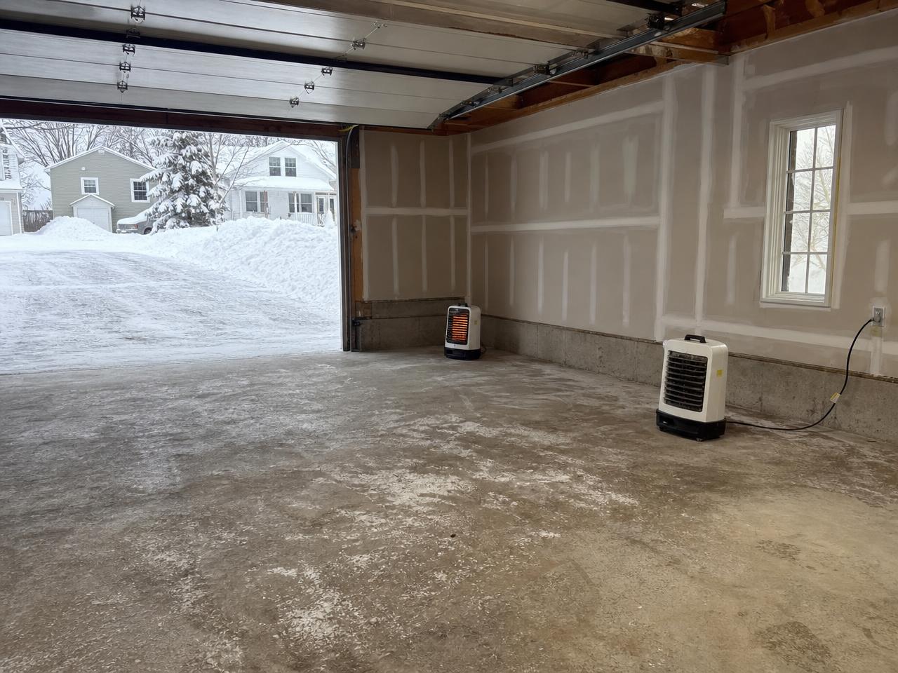 Snowy driveway outside a garage with heaters warming a bare concrete slab